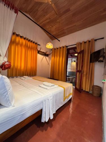 a bedroom with a large bed with yellow curtains at The Elephant Next-Door in Udawalawe