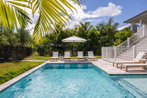 a swimming pool with chairs and an umbrella at Springtide House -Dock & Home w Pool in Stock Island