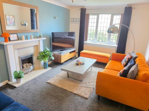 a living room with an orange couch and a television at 4 Bedroom House Near Manchester Airport, Wythenshawe Hospital and Trafford Centre in Wythenshawe