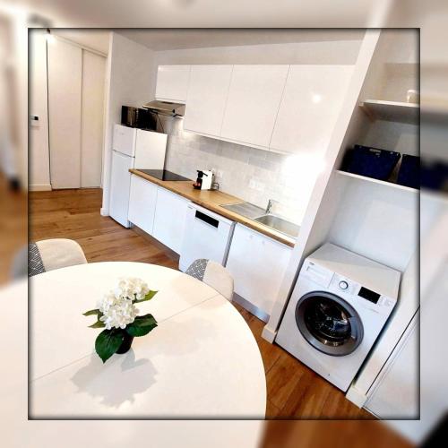 a white kitchen with a table with a vase of flowers at Le Cottage Jardin élégant & cosy, plage pour 6 personnes, animaux admis Biscarrosse in Biscarrosse