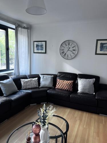 a living room with a black couch and a clock at Chill At Gee's in Nottingham