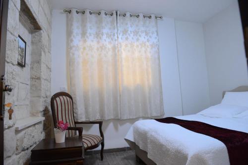 a bedroom with a bed and a chair and a window at Mensa Christi Guesthouse in Nazareth