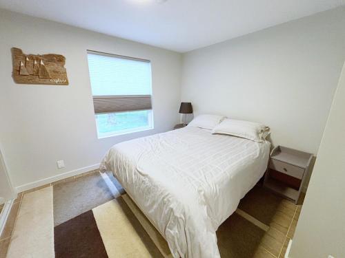 a white bedroom with a bed and a window at Coastal Drift Sooke in Sooke