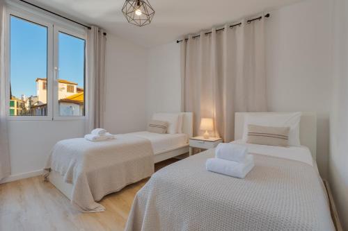 two beds in a white room with a window at Bright 2BR Apartments in Funchal Centre, Walk Everywhere in Funchal