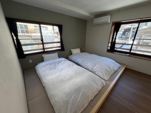 a small bedroom with two beds and two windows at あづまや野沢温泉 in Nozawa Onsen