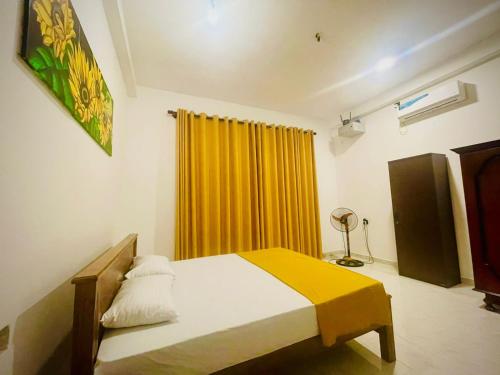 a bedroom with a bed and a yellow curtain at Delmar Homestay in Dickwella