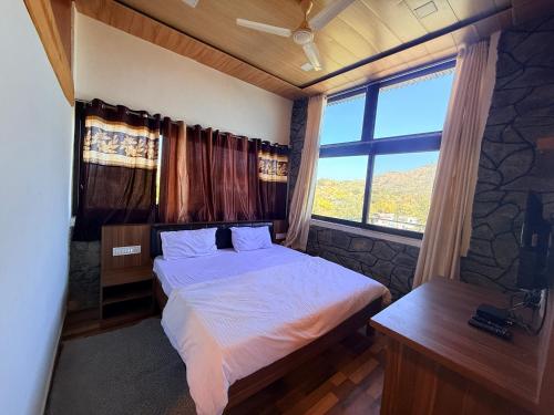 a bedroom with a bed and a large window at Dev Cottage in Mount Ābu