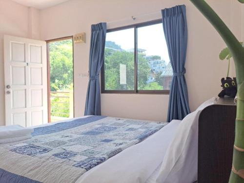 a bedroom with a bed with blue curtains and a window at The Grove Guesthouse in Patong Beach