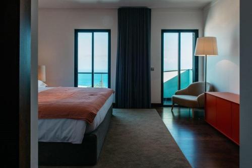 a hotel room with a bed and a chair and windows at Vilas Mediterrâneo in Santa Cruz