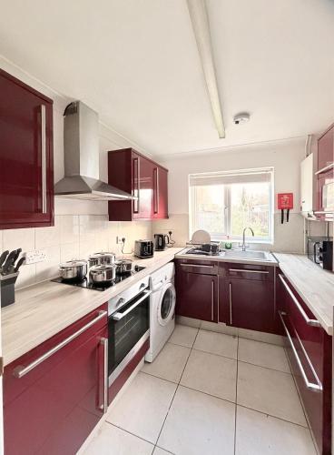 a kitchen with red cabinets and a sink and a dishwasher at Stylish 3BR Cambridge Bungalow, Near Science Park in Cambridge