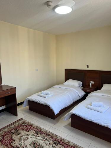 a bedroom with two beds with white sheets and a rug at Badan Suites & Hotel in Amman