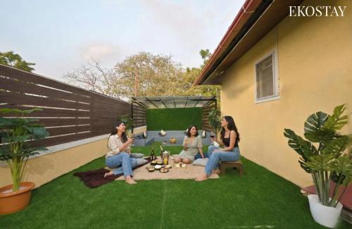 a group of people sitting on the grass in a backyard at EKOSTAY - Pinewood Villa in Alibaug