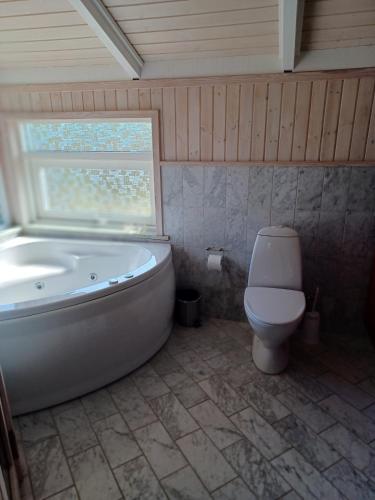 a bathroom with a tub and a toilet and a window at Beautiful cottage on a large natural plot in Ålbæk