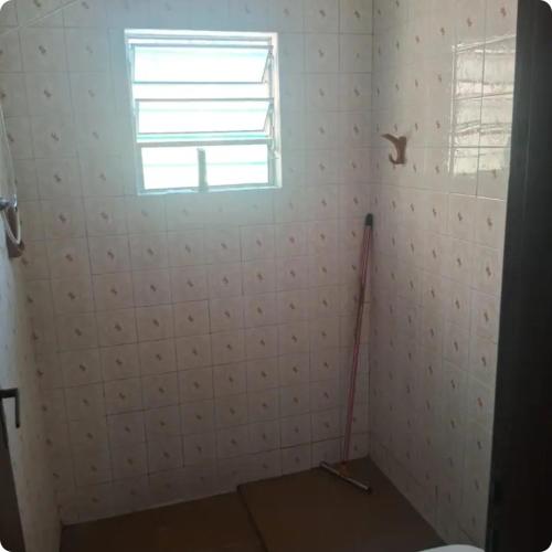 a white tiled bathroom with a window and a mop at Quartos para locação in Mongaguá