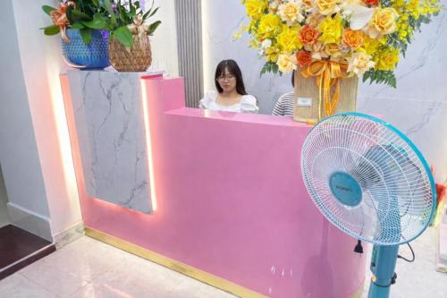 a woman sitting at a pink counter with a fan at PINK Hotel Cần Thơ in Can Tho