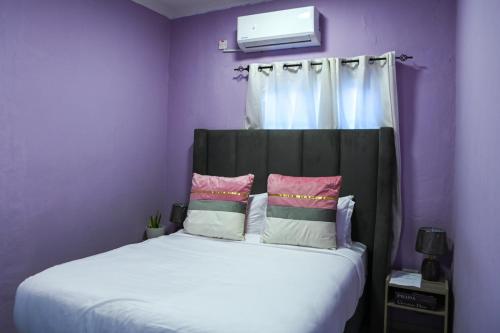a purple bedroom with a bed with a headboard and pillows at Luxe Residence Guest House in Kasane