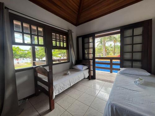 a bedroom with two beds and a balcony with windows at POUSADA BELLA SPIAGGIA in Paraty