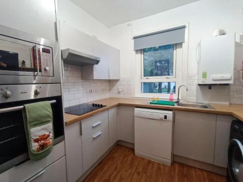 a kitchen with white cabinets and a stove top oven at Funky Cow-Stylish flat near Glasgow Airport in Paisley
