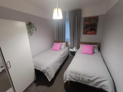 two beds in a small room with pink pillows at Funky Cow-Stylish flat near Glasgow Airport in Paisley