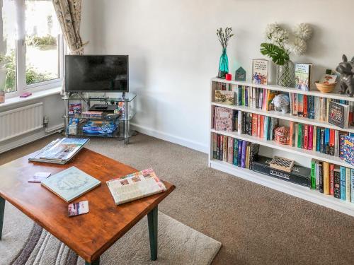 a living room with a table and a book shelf with books at The Hollies in Weston-super-Mare