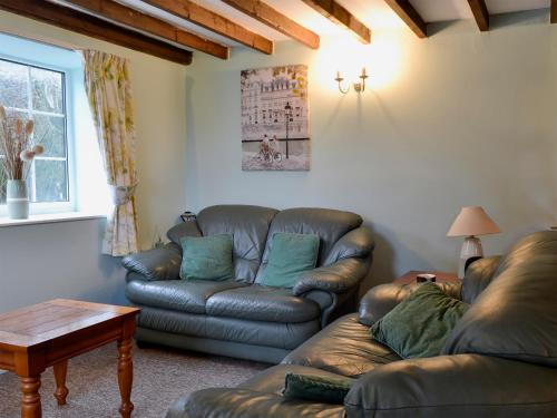 a living room with a leather couch and a table at Commonwealth Cottage in Iron Acton