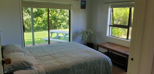 a bedroom with a bed and a table and windows at Lazy Daze at Athenree in Waihi Beach