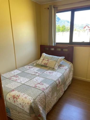 a bedroom with a bed with a quilt and a window at Cabañas Valles del Mañihuales in Villa Maniguales