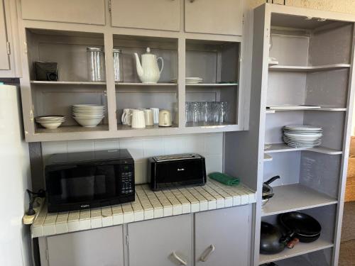 a kitchen with a microwave and some dishes on shelves at Private Rooms at Bayfair in Tauranga