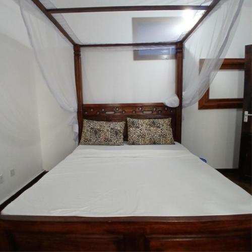 a bedroom with a wooden bed with white sheets and pillows at Tatia apartment in Malindi