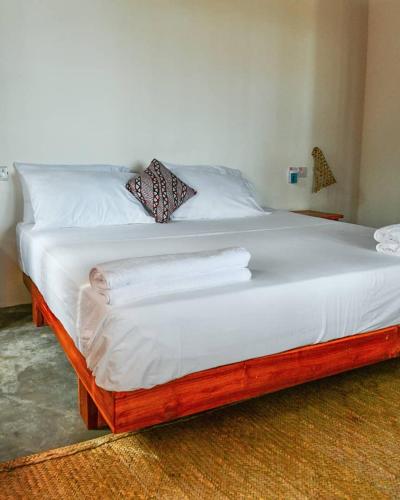 a wooden bed with white sheets and pillows on it at Amani Beach House, Ushongo in Pangani