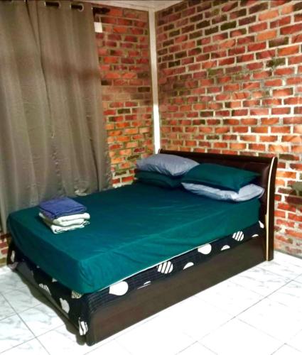 a bed in a brick wall with a green sheets and pillows at Homestay Anjang in Tapah