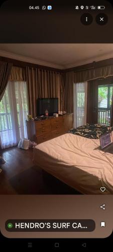 a bedroom with a bed and a tv and windows at HENDRO'S SURF CAMP Pulau merah in Pasanggaran