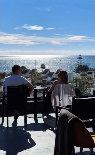 a man and woman sitting at a table near the ocean at The Orange House Boutique Hotel and Upstairs Rooftop Bar Center of La Cala de Mijas 100m from the Beach in La Cala de Mijas