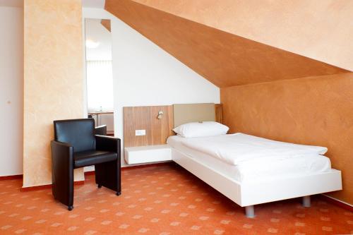 a bedroom with a white bed and a black chair at Hotel & Restaurant Ernst in Giesen