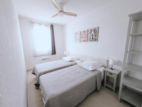 two beds in a white room with a ceiling fan at Maison de vacances près du Mont Ventoux in Aubignan