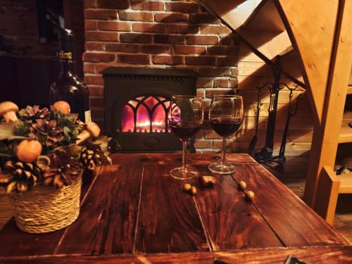 two glasses of wine on a wooden table in front of a fireplace at Wierzbowy Jar- kameralny domek przy lesie w Rudawach Janowickich stworzony dla osób szukających spokoju in Janowice Wielkie