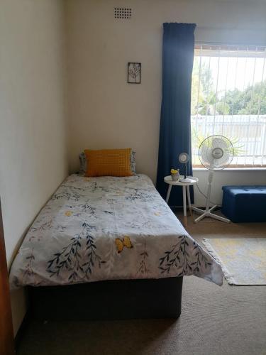 a bedroom with a bed with a blue curtain and a window at Mimosa House Twin Room in Brackenfell