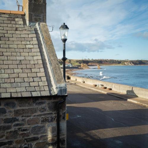 a street light next to a brick building next to the ocean at Sea Crest - Beachfront Escape with Whisky Snug in Cullen
