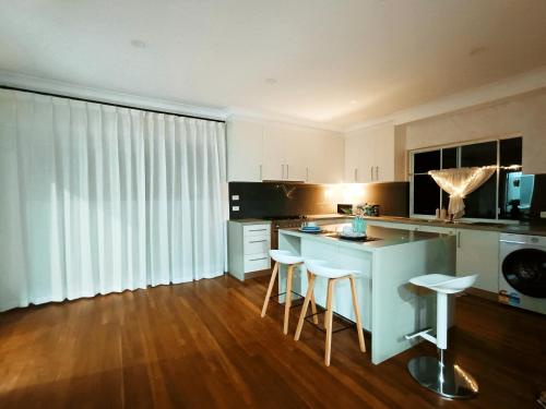 a kitchen with white cabinets and a island with bar stools at Easy access to city park side cosy house in a convenient hub in Sydney