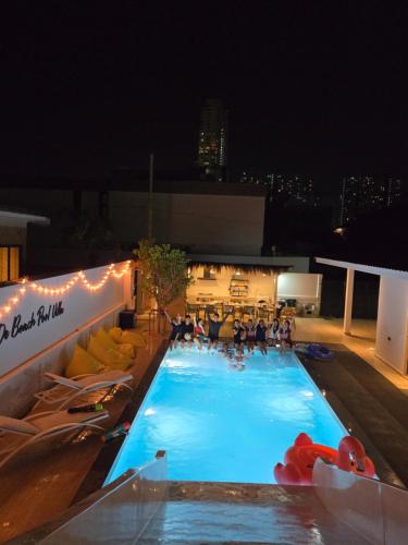 a large swimming pool with people sitting around it at night at De Beach pool villa เดิน 3 นาทีจากชายหาด in Jomtien Beach