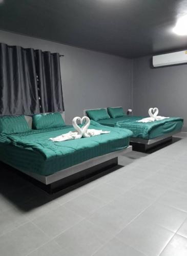 two beds in a room with green sheets and white towels at Dan Mai Homestay in Trat