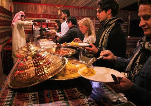 un gruppo di persone in piedi attorno a un tavolo con del cibo di Rum Sky Experiences a Wadi Rum