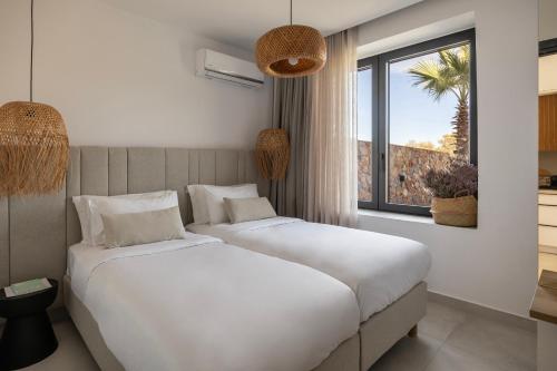 two beds in a hotel room with a window at Norte Luxury Villas in Agioi Apostoli