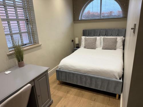 a bedroom with a bed and a desk and two windows at Cosy small cottage in Wirral Merseyside with kitchen in Lower Bebington
