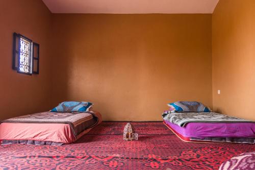 two beds in a room with a red carpet at Sahara Peace in Mhamid