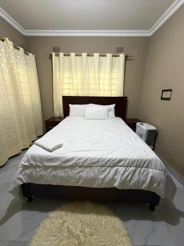 a bedroom with a large bed with white sheets and a rug at Edmut Apartments in Lusaka
