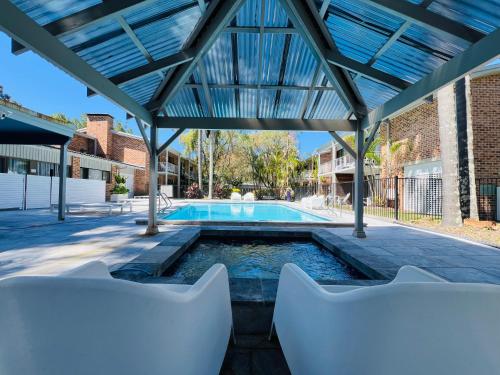 a swimming pool with two white chairs in front of a building at The Select Inn Gosford in Gosford
