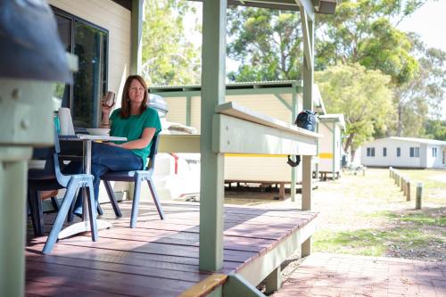 a woman sitting at a table on a porch at Molloy Holiday Park in Kudardup