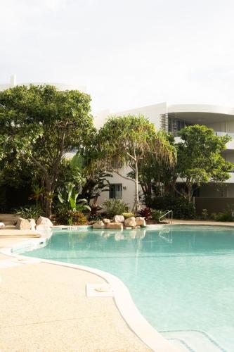 a swimming pool in front of a building with trees at Cotton Beach Resort 1 Bdr Apartment in Casuarina