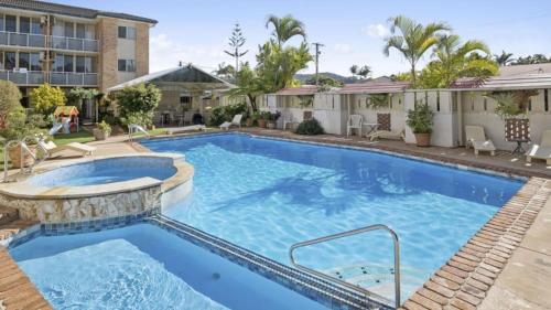 a swimming pool at a resort with a hotel in the background at Priority Beach Stay in Coffs Harbour